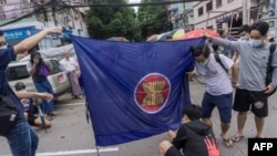 Para pengunjuk rasa bersiap untuk membakar bendera kelompok Perhimpunan Bangsa-Bangsa Asia Tenggara (ASEAN), saat mereka mengambil bagian dalam demonstrasi flash mob menentang kudeta militer di Yangon. (Foto: AFP)