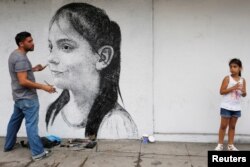 Ariadna Herrera, 6, poses for Cuban artist Maisel Lopez as he paints the wall of a state art gallery in Havana, April 18, 2017.