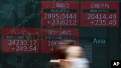 A woman wearing a face mask walks past an electronic stock board showing Japan's Nikkei 225 and other Asian countries' index at a securities firm in Tokyo, May 11, 2020. 