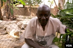Albert Ngendera poses with his pets, eight crocodiles that will soon become over 40 and no longer fit on his porch. (VOA / H. McNeish)
