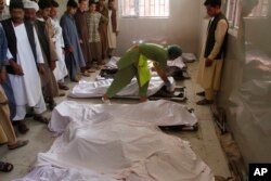 FILE - Men mourn over relatives' bodies in a hospital near the site of an explosion in Herat, Afghanistan, June 6, 2017.