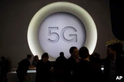 FILE - People stand next to a 5G logo during the Mobile World Congress wireless show, in Barcelona, Spain, Feb. 28, 2018.