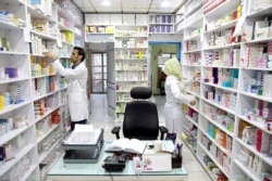 FILE - Pharmacists pick medicine from shelves in a drugstore in downtown Tehran, Iran, June 19, 2019. From imported chemo and other medicines to those made domestically, many Iranians blame shortages on U.S. sanctions.