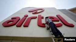 FILE - A worker cleans a logo of Bharti Airtel at its zonal office building in the northern Indian city of Chandigarh.
