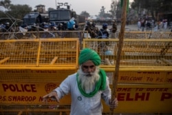 FILE - A farmer stands in front of police barricades during a protest against the newly passed farm bills at Singhu border near Delhi, India, Dec. 3, 2020.
