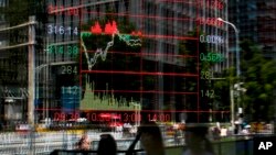 People walk by an electronic board displaying a stock trading index at a brokerage house in Beijing, China, May 24, 2017. 