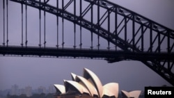 FILE - The sun illuminates the Sydney Opera House as a ferry sails past during a storm at Sydney Harbor in Australia.