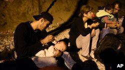 Syrian refugee Abed Hadi,19, feeds his nephew as he sits with other migrants beside railway tracks, waiting to cross the border from Idomeni, in northern Greece, to southern Macedonia, Sept. 1, 2015.