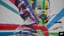 Un hombre con tapabocas pasa junto a un mural del fallecido presidente venezolano Hugo Chávez en Caracas, Venezuela.