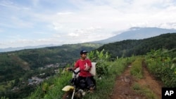 In this March 8, 2017 photo, a farmer rides his motorbike on a dirt road as Gede Pangrango Mountains is seen in the background in Bogor, West java, Indonesia. A sprawling "Trump Community" that will rise next to Gunung Gede Pangrango National Park has alarmed conservationists. They predict that the overall development, including a massive theme park, will overwhelm a refuge for some of Indonesia’s most threatened species. The 3,000 hectare (11.6 square miles) project is the brainchild of President Donald Trump's Indonesian partner, billionaire and presidential hopeful Hary Tanoe.