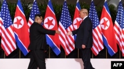 Tổng thống Mỹ Donald Trump (phải) và Lãnh tụ Triều Tiên Kim Jong Un (trái) chìa tay ra bắt tại một hội nghị thượng đỉnh lịch sử của hai nước trên đảo Sentosa của Singapore, ngày 12 tháng 6, 2018.
