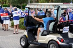 FILE - A voter arrives by golf cart for early voting as others wave signs, in The Villages, Florida, Oct. 7, 2020.
