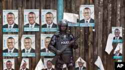 A Ugandan riot policeman blocks the gate of the party headquarters of opposition leader Kizza Besigye, shortly after raiding the premises for the second time in a week, in the capital Kampala, Feb. 22, 2016. 