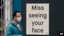 FILE - A man wears a mask while walking past a sign posted on a business in San Francisco, April 11, 2020. The coronavirus outbreak has shut down the U.S. economy.