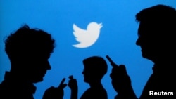 FILE - People holding mobile phones are silhouetted against a backdrop projected with the Twitter logo in this illustration.