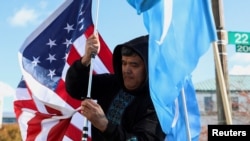 FILE - Zulfikar Mustafa puts up a U.S. flag during a rally in support of Uyghurs outside the State Department in Washington, Nov. 28, 2022. Uyghur Americans report an increase in transnational repression against them by China.