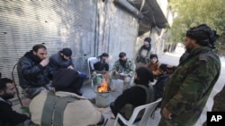 FILE - Rebel fighters of al-Jabha al-Shamiya (Levant Front) warm themselves around a fire near the justice palace in the old city of Aleppo, Syria, Jan. 28, 2016. 