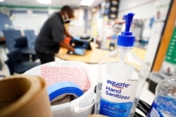 FILE - Hand sanitizer sits on a cart as Des Moines Public Schools custodian Tracy Harris cleans a chair at Brubaker Elementary School, July 8, 2020, in Des Moines, Iowa.