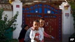 FILE - Uyghur children play while their relatives rest outside their house, which is decorated with Chinese lanterns and barbed wire, at the Unity New Village in Hotan, in western China's Xinjiang region, on Sept. 20, 2018. 