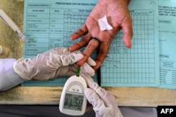 Seorang lansia diambil darahnya untuk pemeriksaan kesehatan hipertensi, kolesterol dan diabetes di Posyandu Banda Aceh, 15 Desember 2021. (CHAIDEER MAHYUDDIN/AFP)