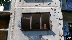 An elderly woman looks out of her apartment window in a building damaged in a May rocket attack in Sloviansk, Donetsk region, eastern Ukraine, Aug. 6, 2022.