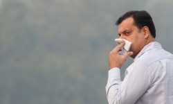A man uses his handkerchief to cover his face as he walks on a road on a smoggy morning in New Delhi, India, Nov. 11, 2019.