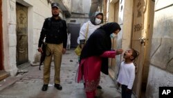 Seorang polisi bertugas mengawal petugas kesehatan saat memberikan vaksin polio kepada seorang anak di Peshawar, Pakistan, Senin, 24 Oktober 2022. (AP/Muhammad Sajjad)