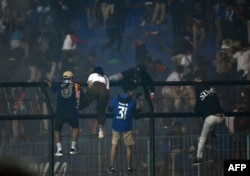 Para penonton memanjat pagar di dekat tribun penonton di tengah desak-desakan maut usai pertandingan sepak bola antara Arema FC dan Persebaya di stadion Kanjuruhan di Malang, Jawa Timur (Foto: AFP)