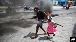 FILE - A woman guides a child past a demonstration against increasing violence in Port-au-Prince, Haiti, March 29, 2022. This week, an armed group pulled a critically ill patient from an ambulance and shot him dead in the street.  