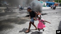 FILE - A woman guides a child past a demonstration against increasing violence in Port-au-Prince, Haiti, March 29, 2022.