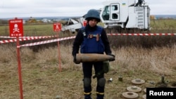 A Ukrainian service member holds a display munition during a mine-clearing demonstration with the Armtrac 400 demining machine in the background, in the Kharkiv region, Oct. 27, 2022. 