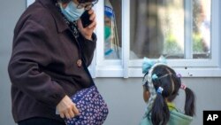 A worker wearing a protective suit waits to administer COVID-19 tests to a woman and girl at a coronavirus testing site in Beijing, Oct. 19, 2022.