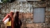 FILE - Women walk in front of a metal fence made of vegetable oil cans from USAID at the Dadaab refugee complex, northeastern Kenya, on April 18, 2018. 