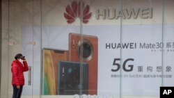 FILE - A woman wearing a mask against COVID-19 stands near an advertisement for Huawei mobile phones in Beijing, March 8, 2020.