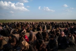 FILE - Men wait to be screened by U.S.-backed Syrian Democratic Forces (SDF) fighters after being evacuated out of the last territory held by Islamic State militants, near Baghuz, eastern Syria, Feb. 22, 2019.