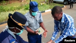 Police officers show a visitor how to disinfect his hands against the spread of coronavirus disease at State House in Harare, Zimbabwe, March 19, 2020.