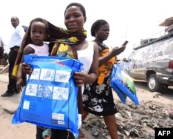 FILE - A woman carrying a baby holds a treated mosquito net during a malaria prevention event at Ajah in Eti Osa East district of Lagos, Nigeria, April 21, 2016.