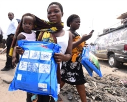 FILE - A woman carrying a baby holds a treated mosquito net during a malaria prevention action at Ajah in Eti Osa East district of Lagos, Nigeria, April 21, 2016.