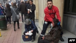 A private security guard helps a wounded women outside the Maalbeek metro station in Brussels on March 22, 2016 after a blast at this station located near the EU institutions.