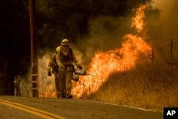 Firefighters light a backfire while trying to keep a wildfire from jumping Santa Ana Road near Ventura, Calif., Dec. 9, 2017.