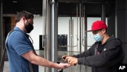A Trader Joe's store employee, right, sprays hand sanitizer on a customer before he enters the Brooklyn supermarket, in New York, June 30, 2020.