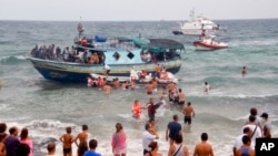 FILE - Vacationers join Italian Coast Guard officers to help migrants from Eritrea ashore near the seaport of Siracusa after a long and treacherous journey, Aug. 15, 2013.