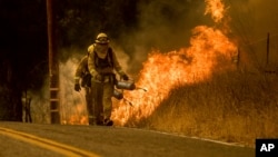 Firefighters light a backfire while trying to keep a wildfire from jumping Santa Ana Road near Ventura, Calif., Dec. 9, 2017. 