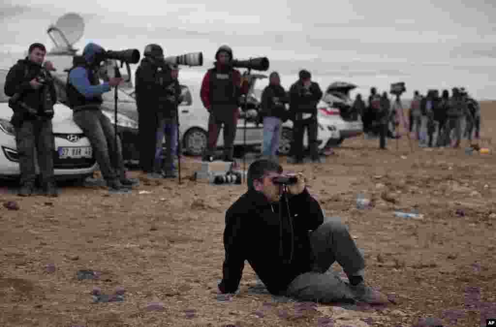 A man, backdropped by members of the media, sits on a hilltop on the outskirts of Suruc watching the fighting between Syrian Kurds and the militants of Islamic State group in Kobani, Syria, Oct. 19, 2014.
