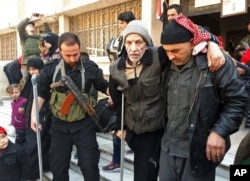 FILE - This photo released by the Syrian official news agency SANA shows a Syrian government soldier, left, helping a civilian who'd fled from fighting between the Syrian government forces and rebels, at an army checkpoint in eastern Ghouta, a suburb of Damascus, Syria, March 13, 2018.