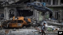 A boy rides his bike past destroyed cars and houses in a neighborhood recently liberated by Iraqi security forces, on the western side of Mosul, Iraq, Sunday, March 19, 2017.