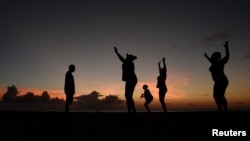 FILE - Women exercise in front of a trainer (L) as the sun sets near Kensington Oval in Bridgetown, Barbados, March 13, 2014. 