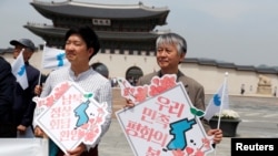 People hold Korean Unification Flags during a pro-unification rally ahead of the upcoming summit between North and South Korea in Seoul, Apr. 26, 2018. The signs read, "Welcome inter-Korean summit" (L) and "Peaceful spring for our people" (R).