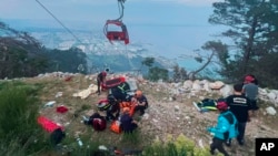 Miembros de los servicios de rescate y emergencia atienden a pasajeros de la cabina de un teleférico que chocó con un poste, lanzándolos a una zona montañosa, a las afueras de Antalya, Turquía, cerca de la noche del viernes 12 de abril de 2024.
