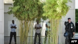 FILE - Security staff believed to be part of Cameroonian president's guard stand next to a Swiss riot police at the entrance of the five-star Intercontinental Hotel during demonstrations against the presence of Cameroon President in Geneva, June 29, 2019.
